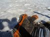 Das Bild zeigt Wanderschuhe mit speziellen Aufsätzen für Eis. Im Hintergrund Schnee. Es scheint die Sonne.